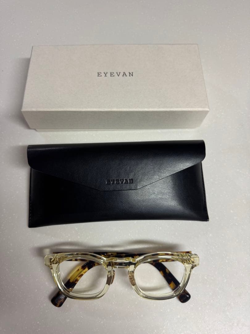 EYEVAN clear tortoiseshell plastic eyeglasses displayed below a black case and white EYEVAN box on a light surface.