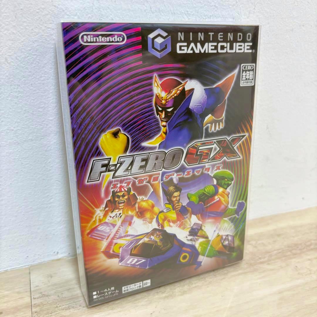 Sealed F‑ZERO GX Nintendo GameCube game box standing upright against a white wall on a wood floor.