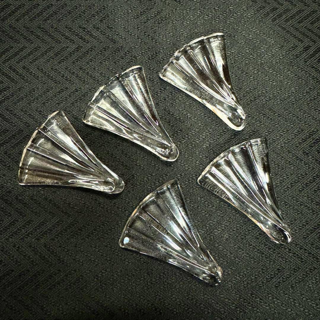 Five clear fan-shaped glass chopstick rests arranged on a dark textured surface.