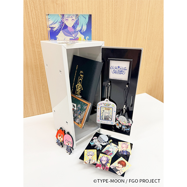 Photograph of the カルデア学園 ミニロッカー white mini locker box opened on a table with character keychains and pins displayed inside and around it.