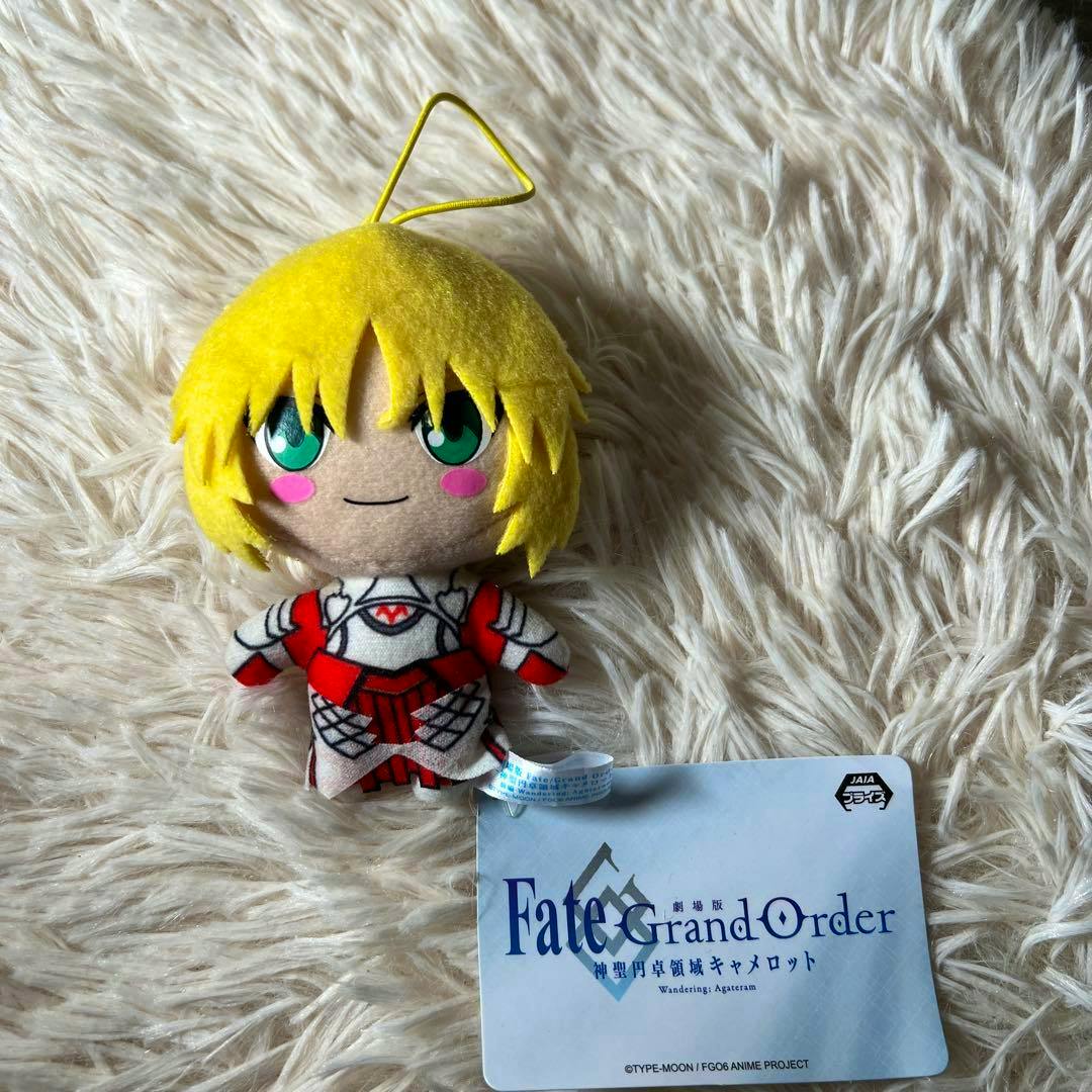 Front view of the FGO (Fate/Grand Order) mascot Mordred plush keychain with yellow hair and green eyes and attached tag on a fluffy background.
