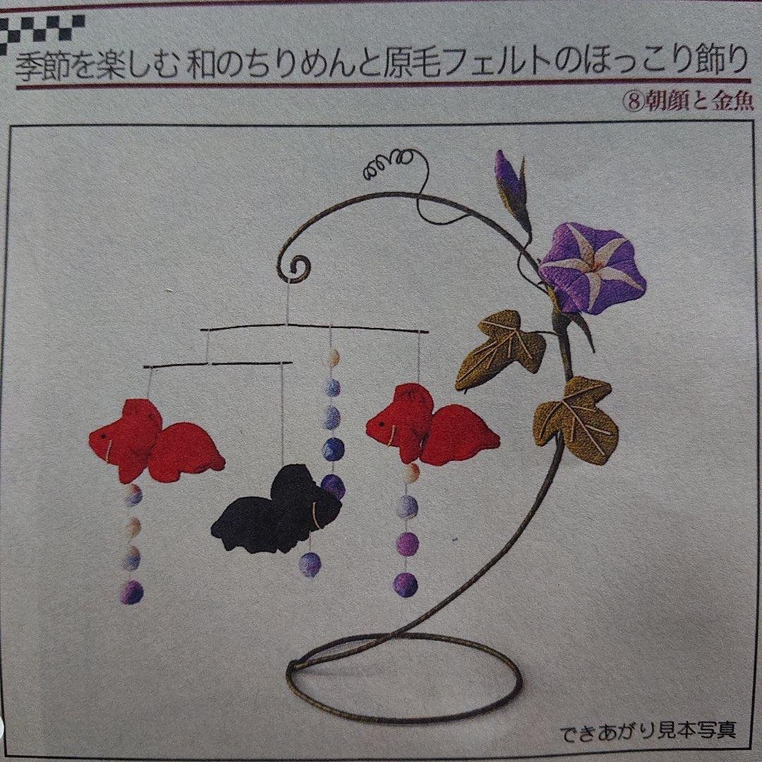 A fabric ornament mobile with hanging fish shapes and felt bead strings on a curling metal stand decorated with a purple fabric flower.