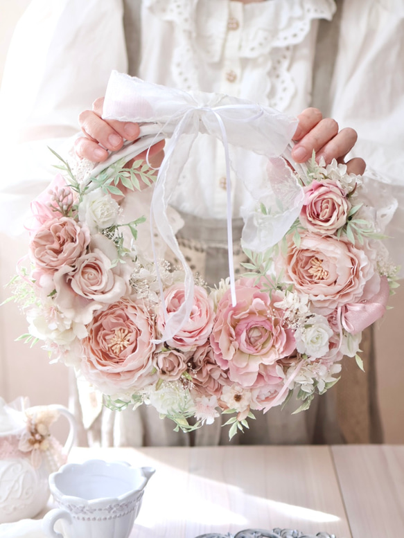 Hands holding a feminine pink half wreath decorated with pink flowers and a white bow.