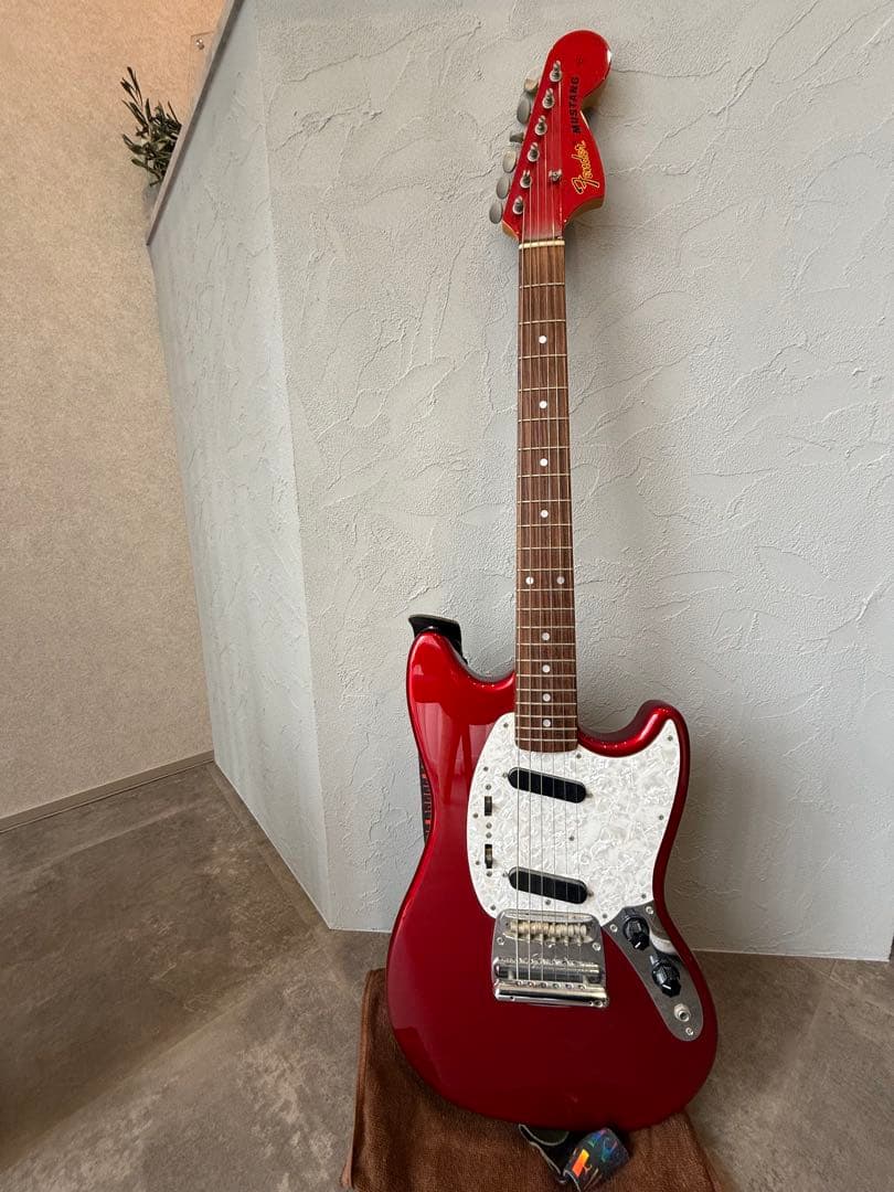 Red MG69 Fender Japan Mustang bass guitar leaning against a textured interior wall.