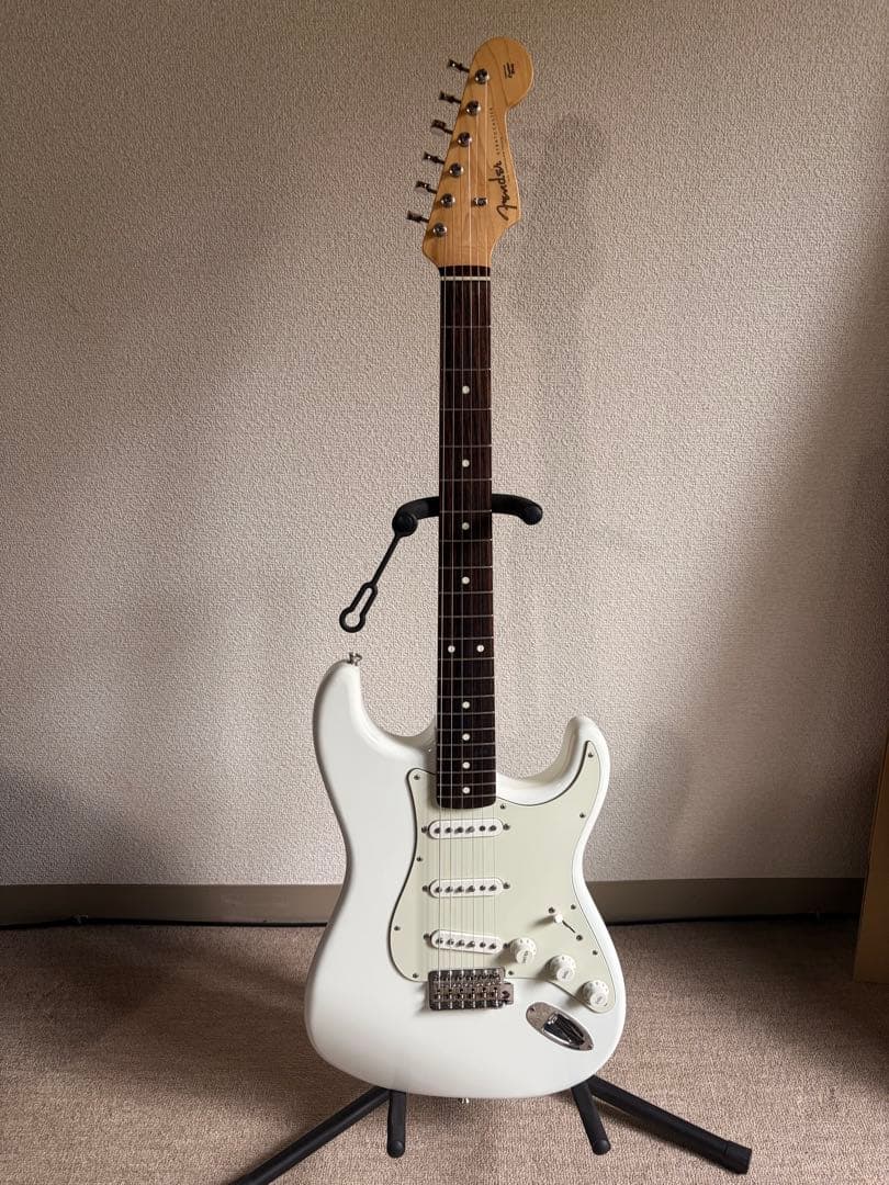 White Fender MIJ Traditional '60s Stratocaster electric guitar on a stand against a wall.