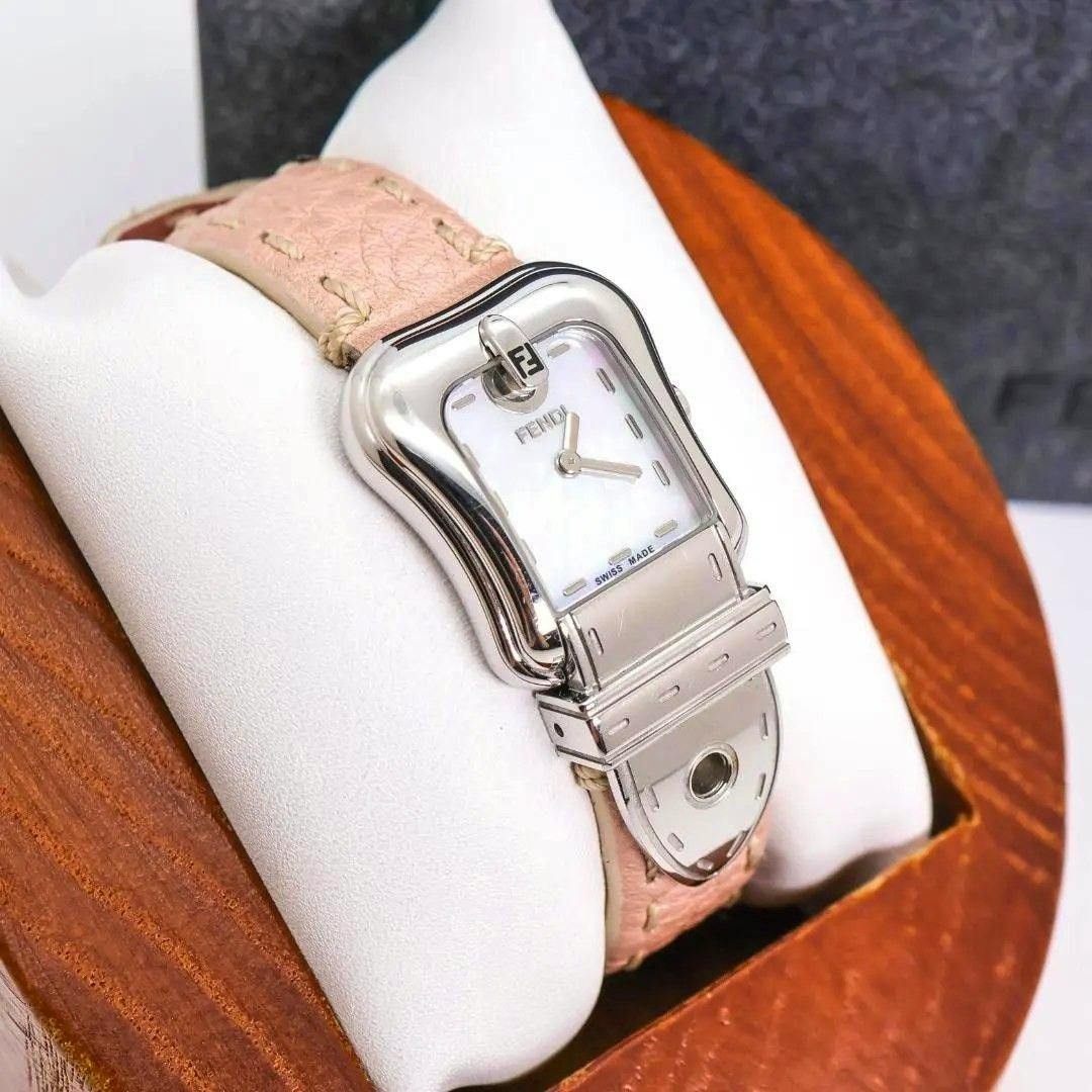 Silver Fendi metal-cased wristwatch with a mother-of-pearl dial and pink leather strap displayed on a white pillow and wooden box.
