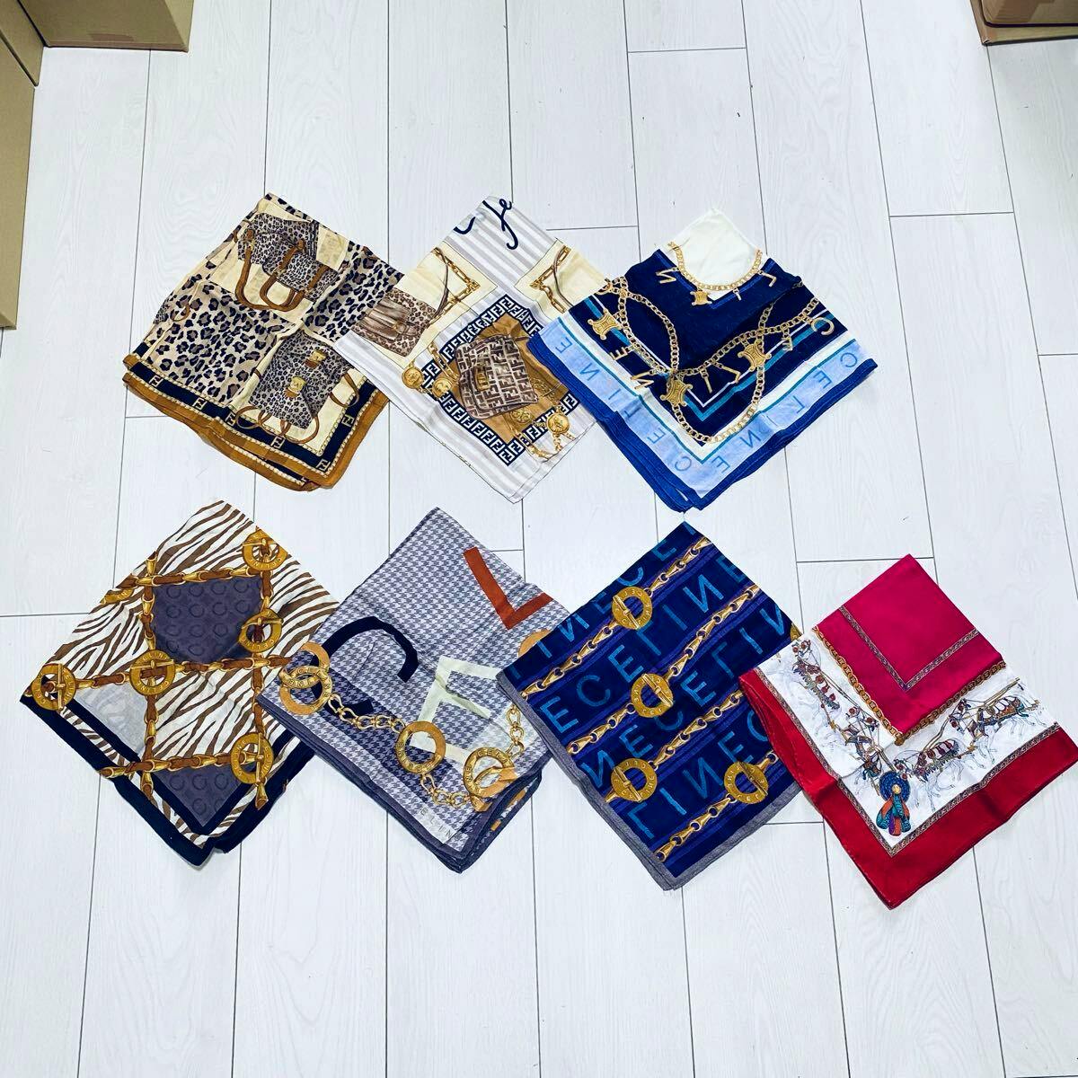 Seven folded handkerchiefs/scarves arranged on a white wooden floor, showing various printed patterns and colors.