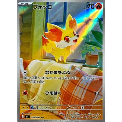 Photograph of the trading card 'フォッコ' showing the full card artwork of the Pokémon character on a blanket by a window, with Japanese text and HP 70.