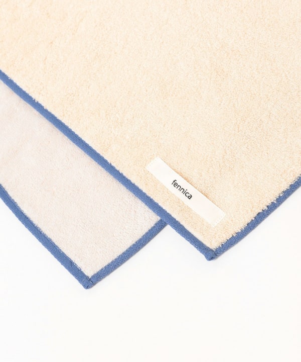Close-up of a fennica cotton bath towel corner showing cream terry fabric, blue edge trim, and the sewn fennica label.