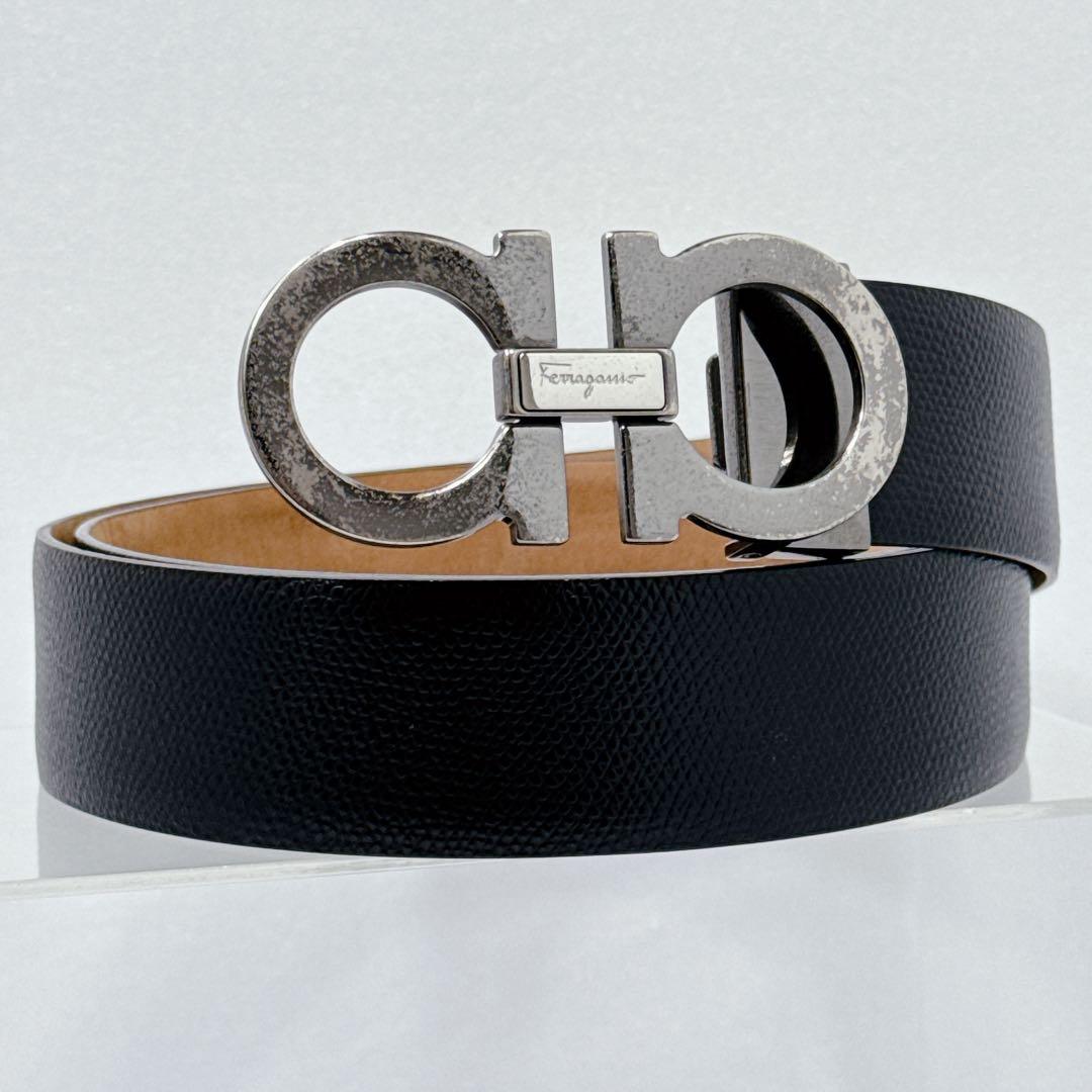 Black textured cow leather Ferragamo belt with a gunmetal double Gancini buckle coiled for display.