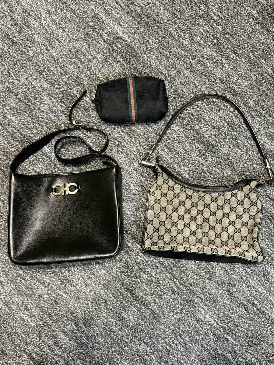 Three bags and pouches on a gray carpet: a black leather shoulder bag with metal hardware, a small black pouch with a green-red stripe, and a beige GG monogram canvas shoulder bag.