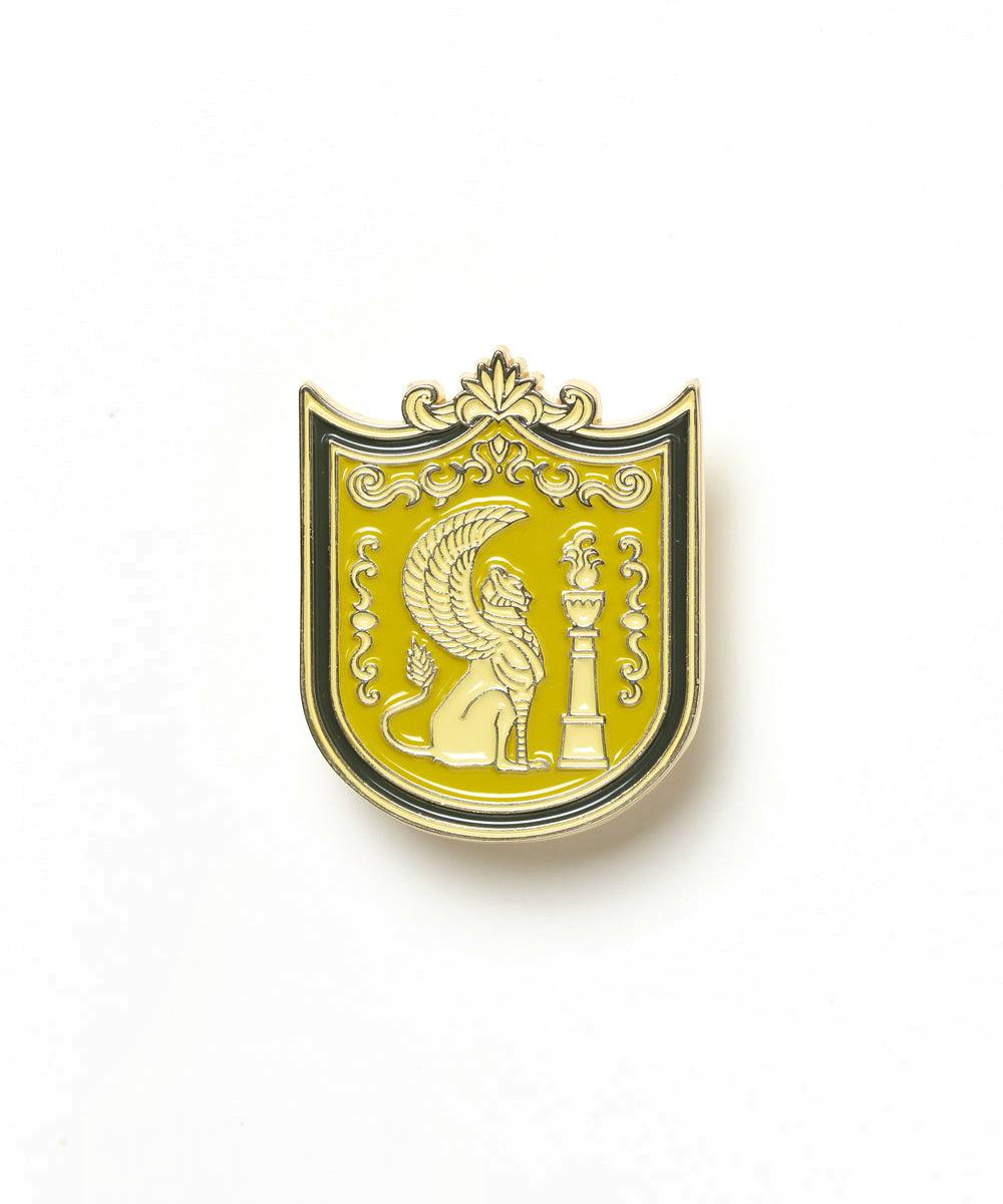Yellow shield-shaped enamel pin showing a winged lion beside a column on a white background.