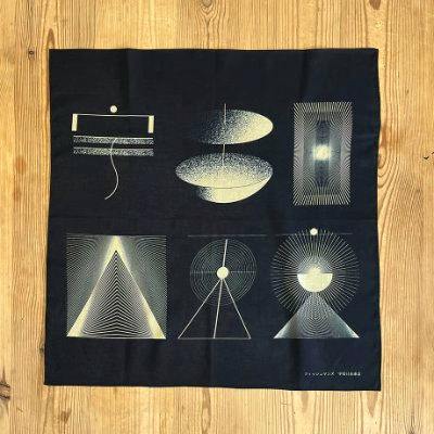 A cotton bandana laid flat on a wooden surface showing a dark background printed with six light-colored geometric designs.
