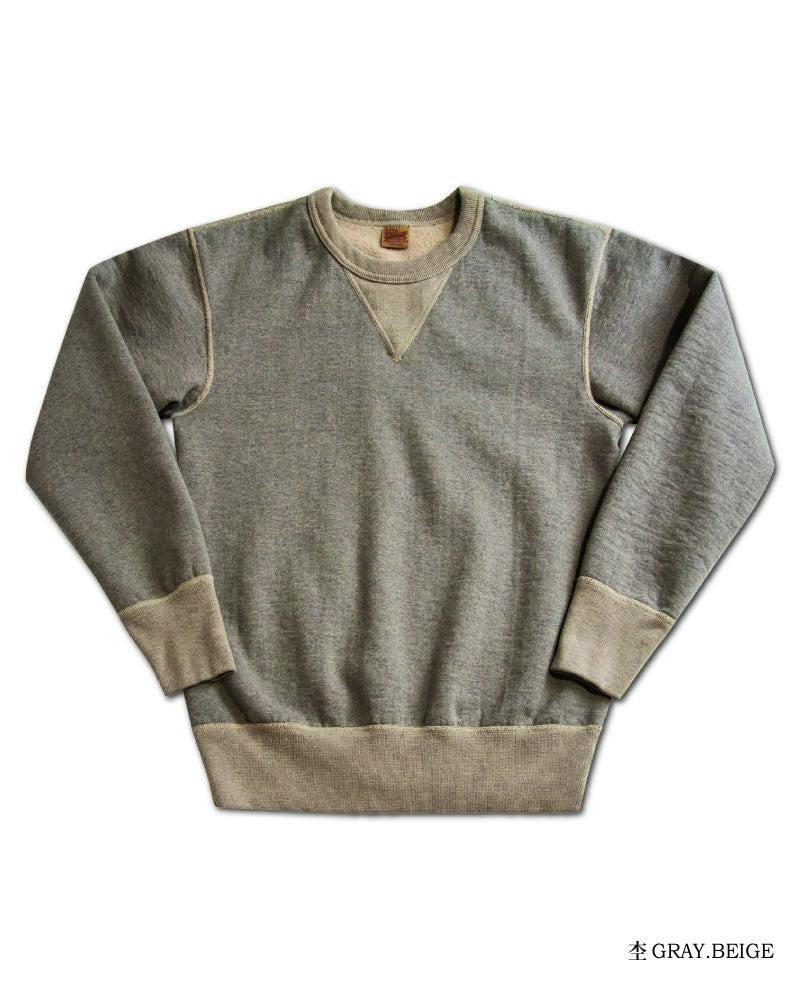 Flat-lay gray-beige cotton crewneck sweater laid flat showing long sleeves, ribbed cuffs and hem, and triangular stitch detail at the neckline.