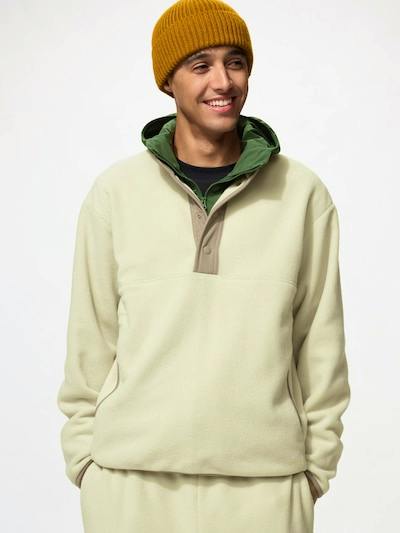 Model wearing a light beige fleece button-snap pullover with a contrasting tan placket and green hood lining.