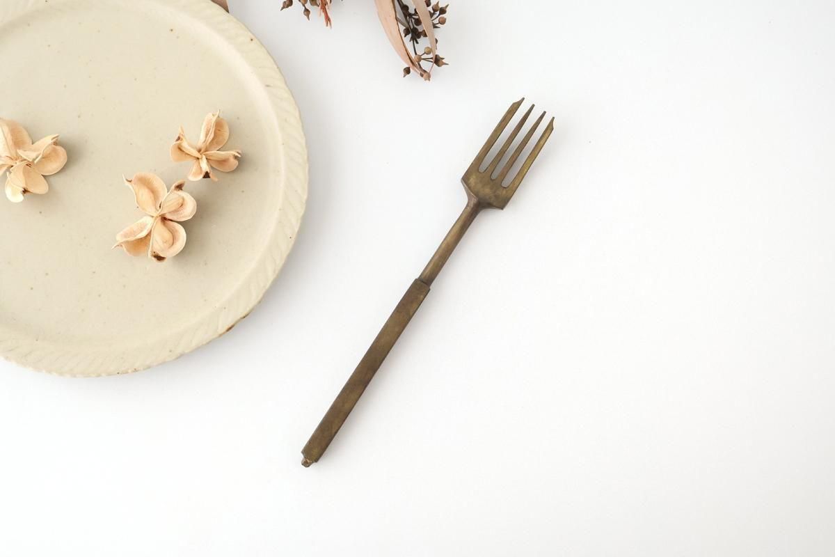 Antique metal fork laid on a white background next to a small plate and dried flowers.