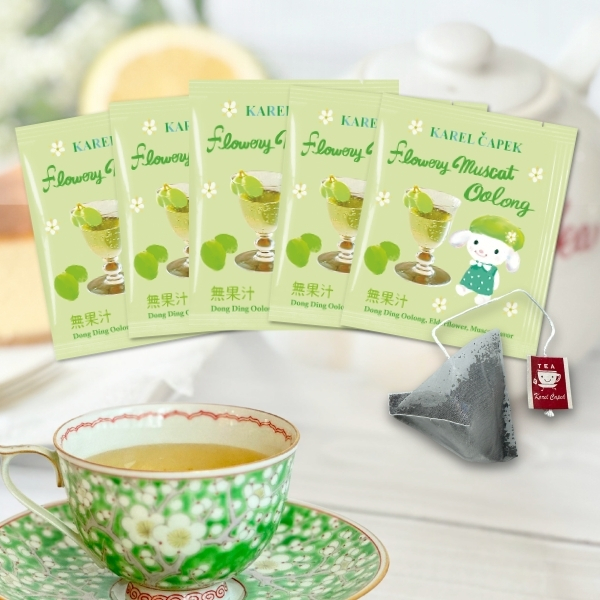 Five Flowery Muscat Oolong tea bag packets fanned behind a pyramid tea bag and a green patterned teacup of brewed tea.