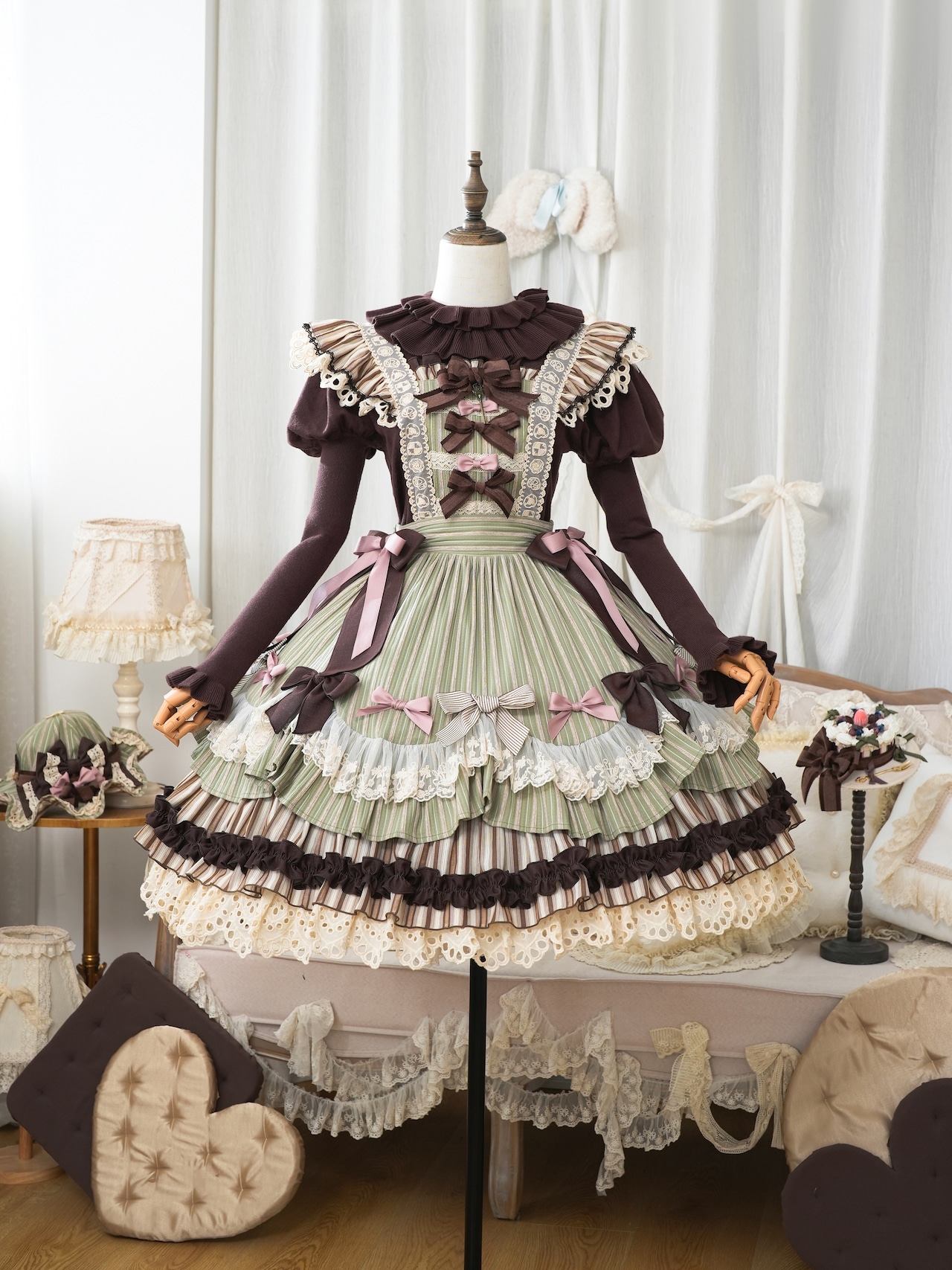 Mannequin displaying a green and brown layered suspender skirt dress with bows and lace in a room setting.