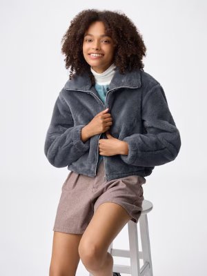 Woman seated on a stool wearing a dark gray fluffy polyester blouson jacket.