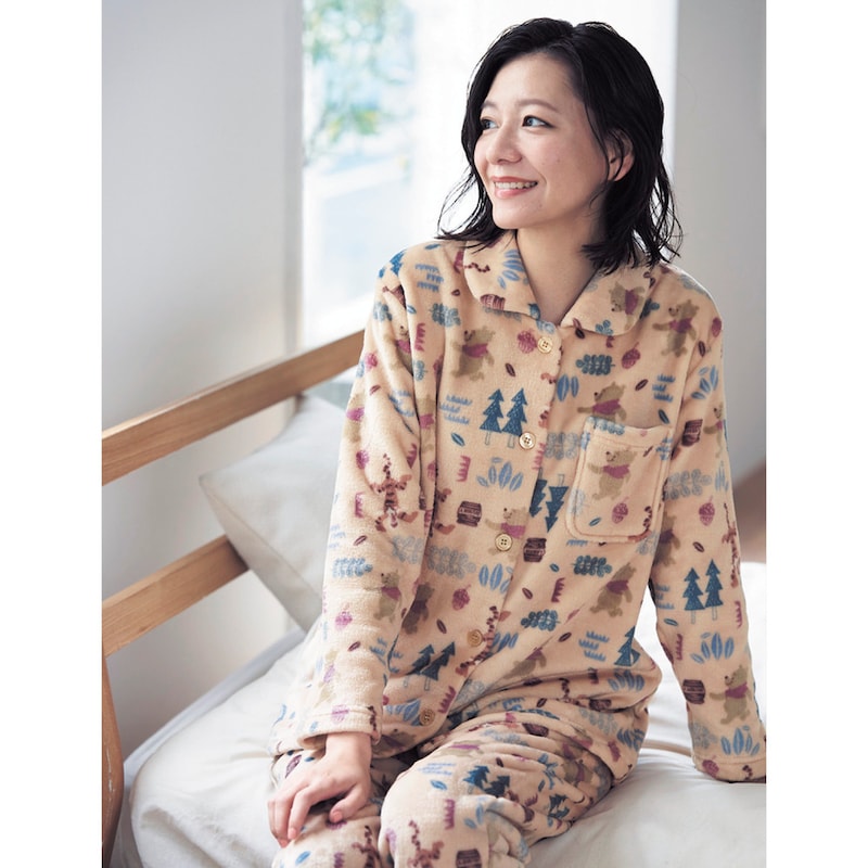 A woman sitting on a bed wearing beige patterned fluffy women’s pyjamas.