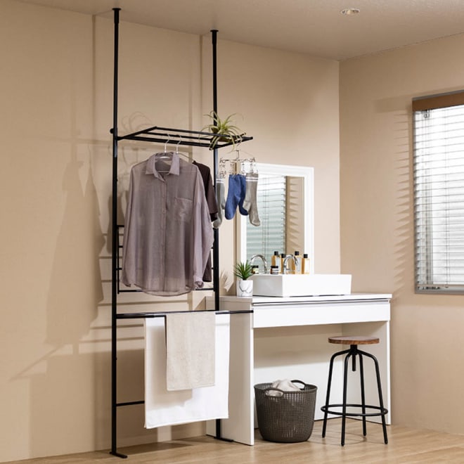 Tension ladder-style hanging rack (stainless steel) installed in a room holding clothes and towels.