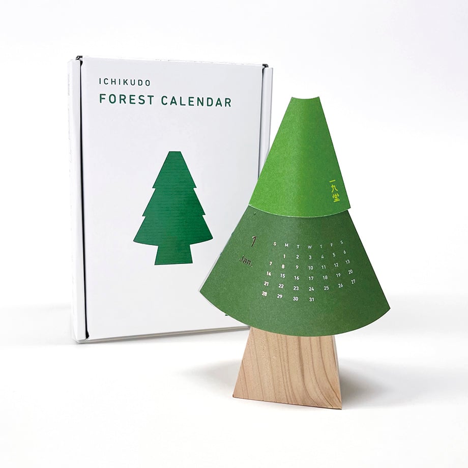 Assembled Forest Calendar desk calendar shaped like a green paper tree on a wooden base with the product box behind it.