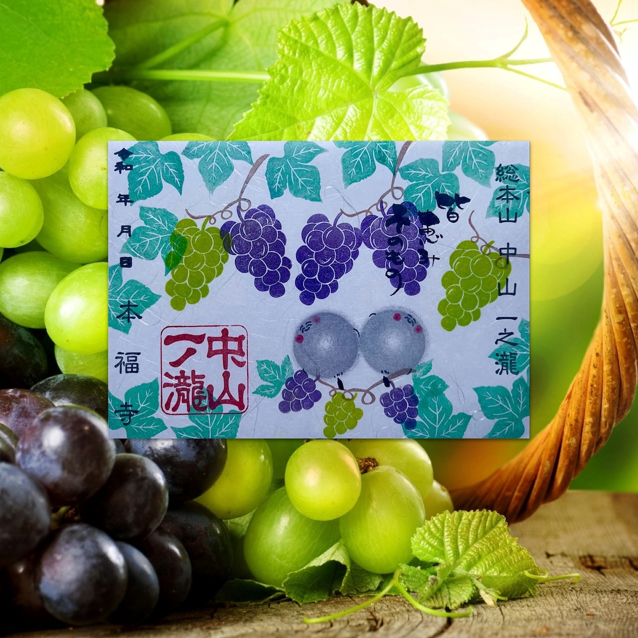 A greeting card depicting illustrated grape clusters and Japanese text placed on a basket of green and purple grapes.