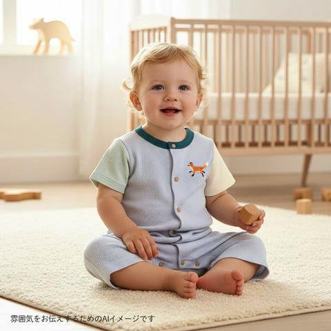 A baby sits on a rug in a nursery wearing the light-blue fox waffle color-block romper shown in the product title.