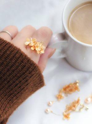 Hand wearing the ring with an orange floral bouquet design beside a cup of coffee.