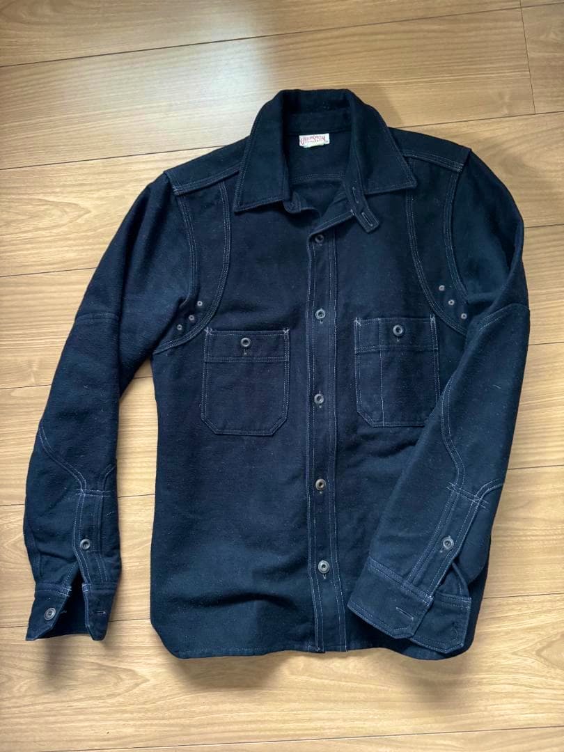 Freewheelers Hammersmith work shirt (size 14) in black laid flat on a wooden floor showing the front, chest pockets, and buttons.