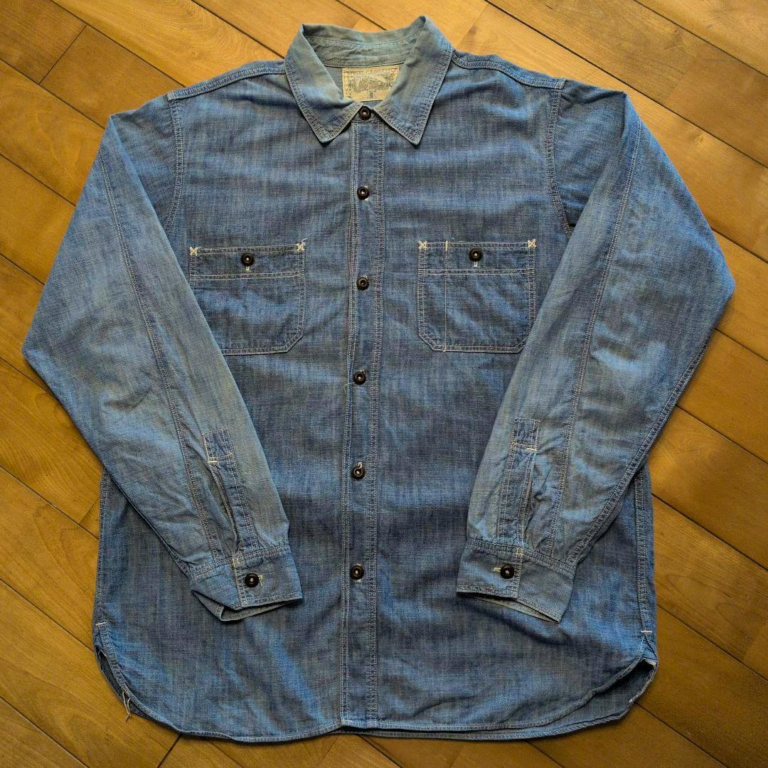 Men's cotton chambray shirt laid flat showing the front with collar, button placket, two chest pockets, and long sleeves.