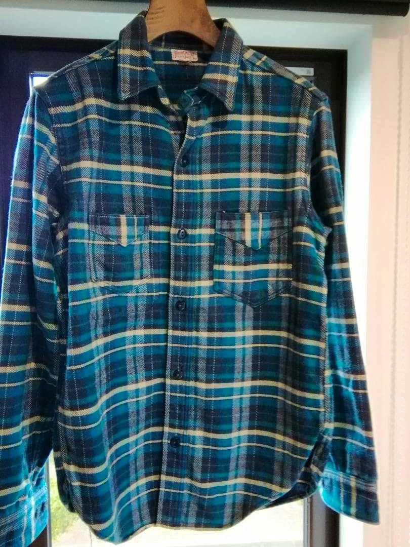 Front view of a men's blue-green plaid cotton flannel shirt hanging on a wooden hanger.