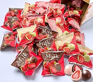 A pile of individually wrapped whole strawberry chocolates in red, brown, and cream wrappers, with a few unwrapped pieces showing the freeze-dried strawberry center.