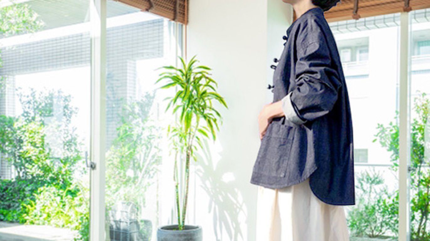 Side view of a model wearing the women's cotton French China jacket indoors by a window with a plant.