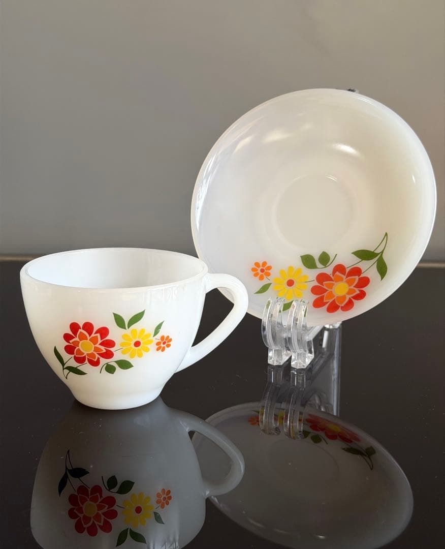 White Arcopal cup and matching saucer with red and yellow Bavaria-style floral pattern displayed on a reflective dark surface.