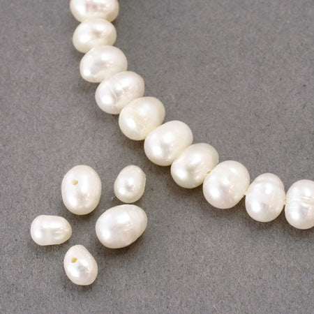 Close-up of white freshwater potato pearls with a short strung section and several loose pearls on a gray background.