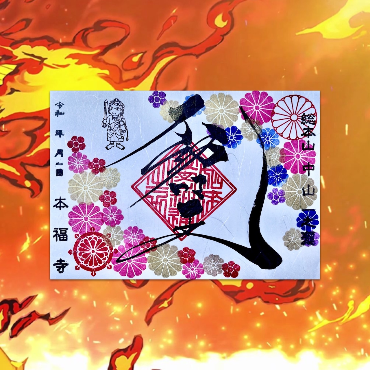 Photo of the greeting card showing the 不動明王御朱印 design with chrysanthemum crest and colorful floral stamps on a fiery background.