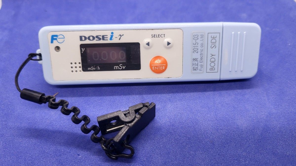 Front view of a pale blue DOSEi-γ personal dosimeter showing its digital display, control buttons, and attached coiled clip.