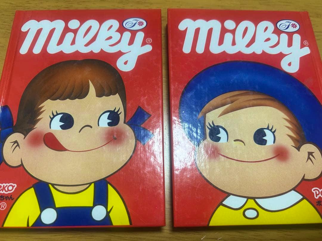 Two red Milky-themed notebooks showing Peko-chan (left) and Poko-chan (right) characters placed side by side on a wooden surface.