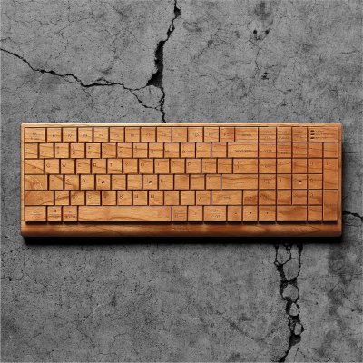 Top-down view of the full wooden wireless PC keyboard with English key layout and wrist rest on a cracked concrete surface.