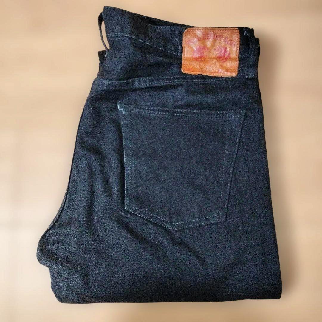 Folded dark denim pants showing the back pocket and leather brand patch.