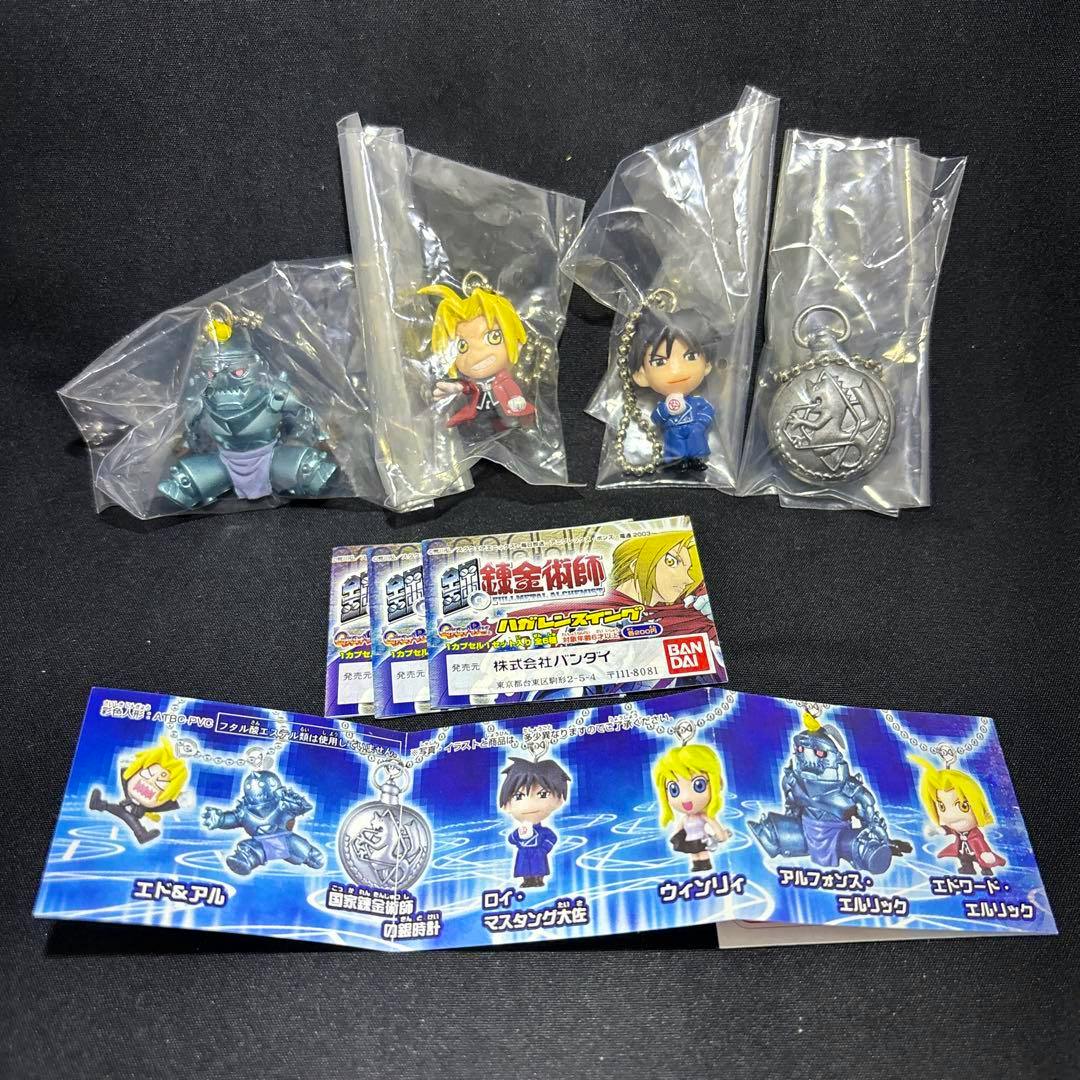Four Fullmetal Alchemist swing keychain figures in sealed plastic bags displayed with a folded character insert on a black background.