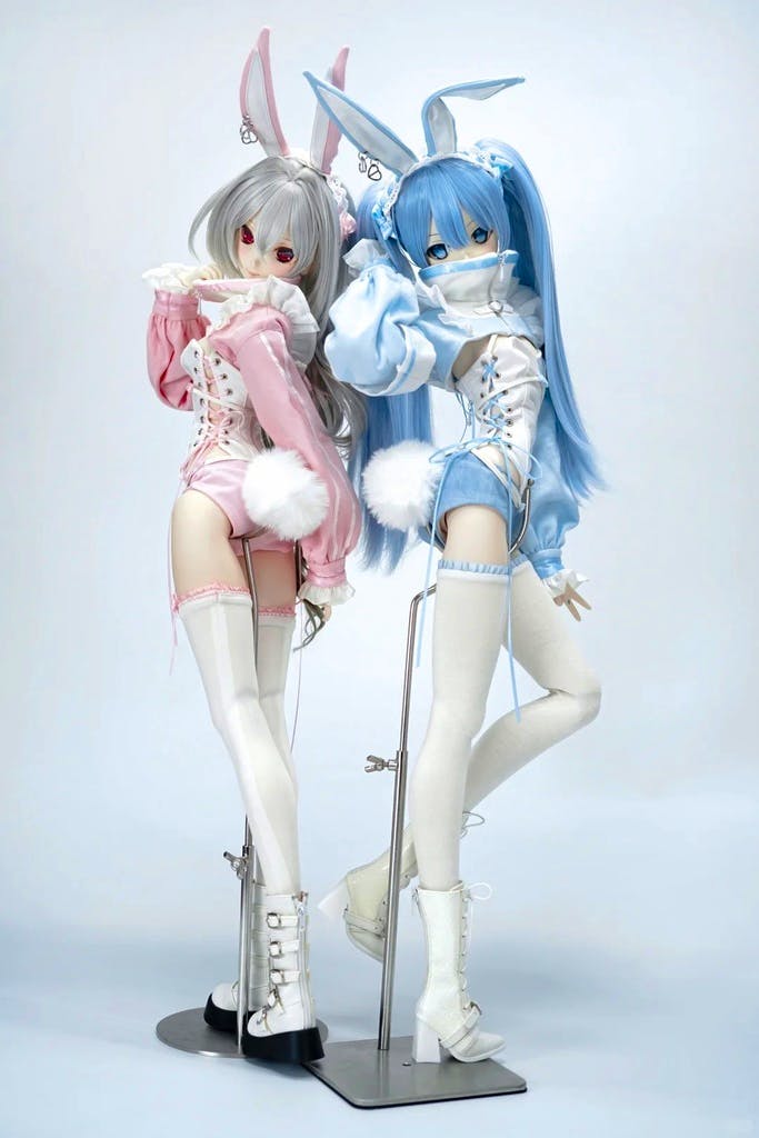 Two 1/4-scale dolls wearing bunny-themed corset outfits in pink and blue with thigh-high stockings and bunny ears, posed on stands.