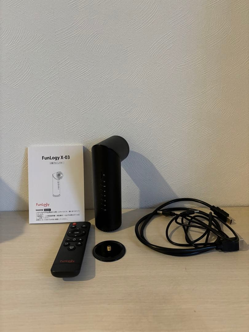 FunLogy X-03 projector body displayed with remote, user manual, base, and cables on a table.
