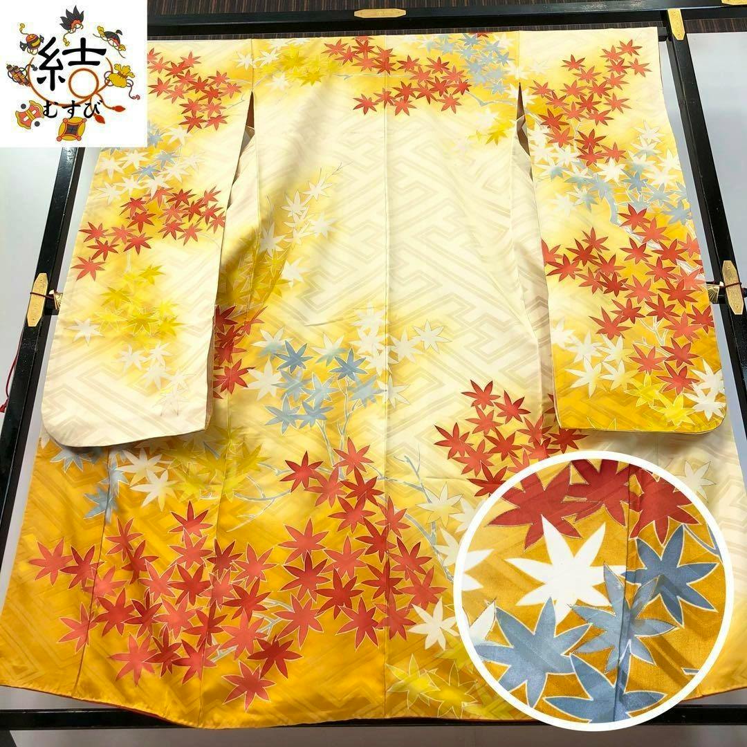 A pale yellow furisode kimono with red, blue, white, and yellow maple-leaf floral patterns displayed flat on a frame.