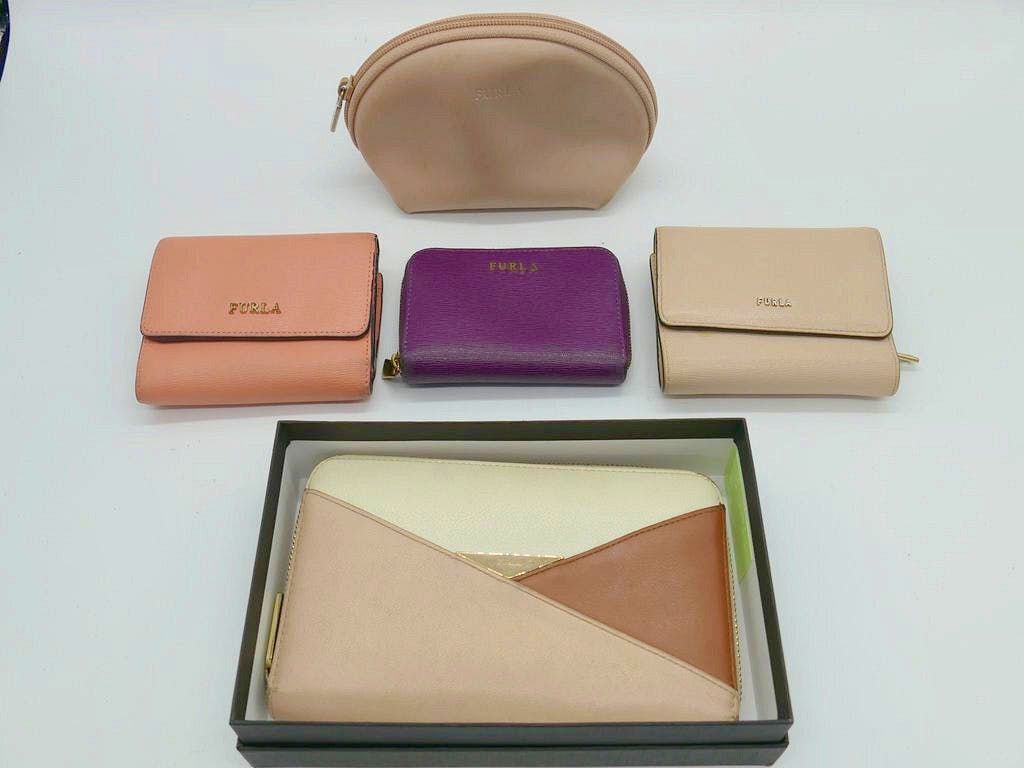 Five Furla women's wallets and pouches of various colors arranged on a white background, including a long zip wallet in a box and three smaller wallets and a pouch.