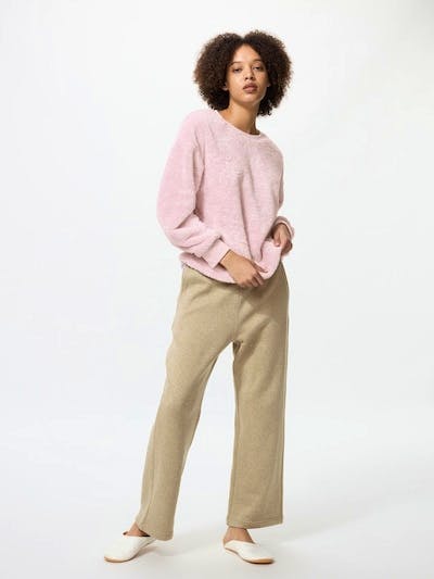 Model wearing a pink furry fleece pajama top and beige fleece pajama pants on a white background.