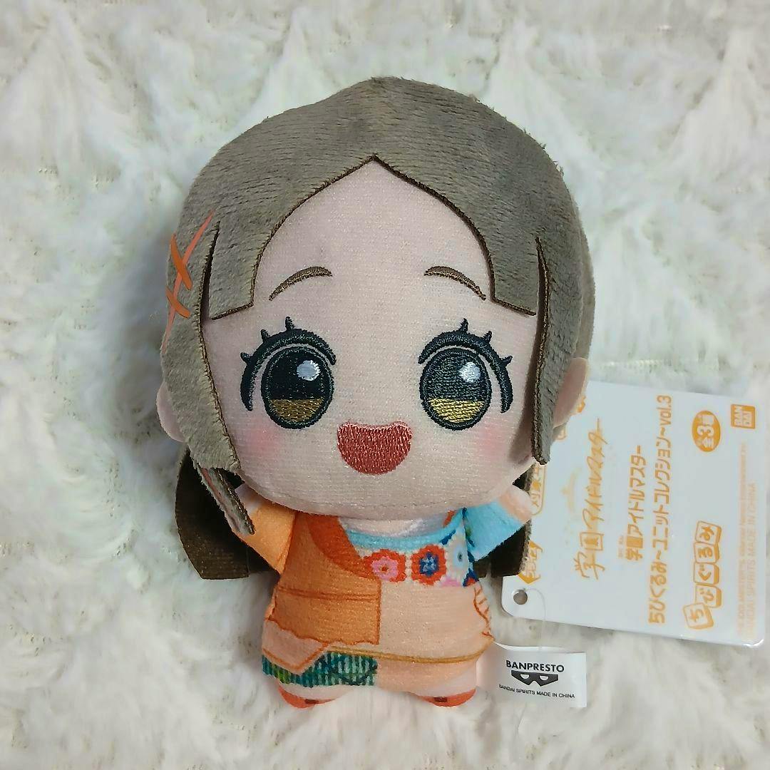 Frontal view of the chibi plush (学園アイドルマスター≪倉本千奈≫) with an embroidered face and visible tag on a white fur background.