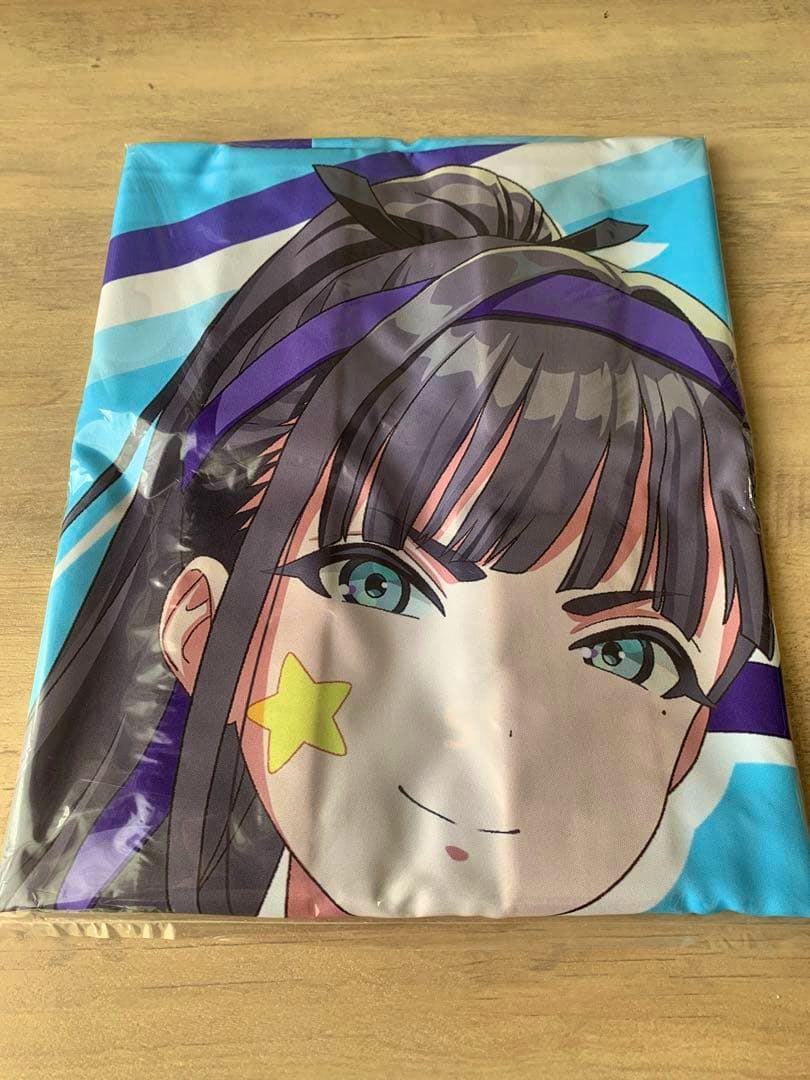 Folded polyester happi in plastic packaging showing a large printed anime character face on a wooden surface.