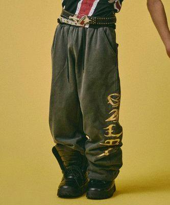 Model wearing men's cotton sweatpants with gold vertical lettering on the leg against a yellow background.